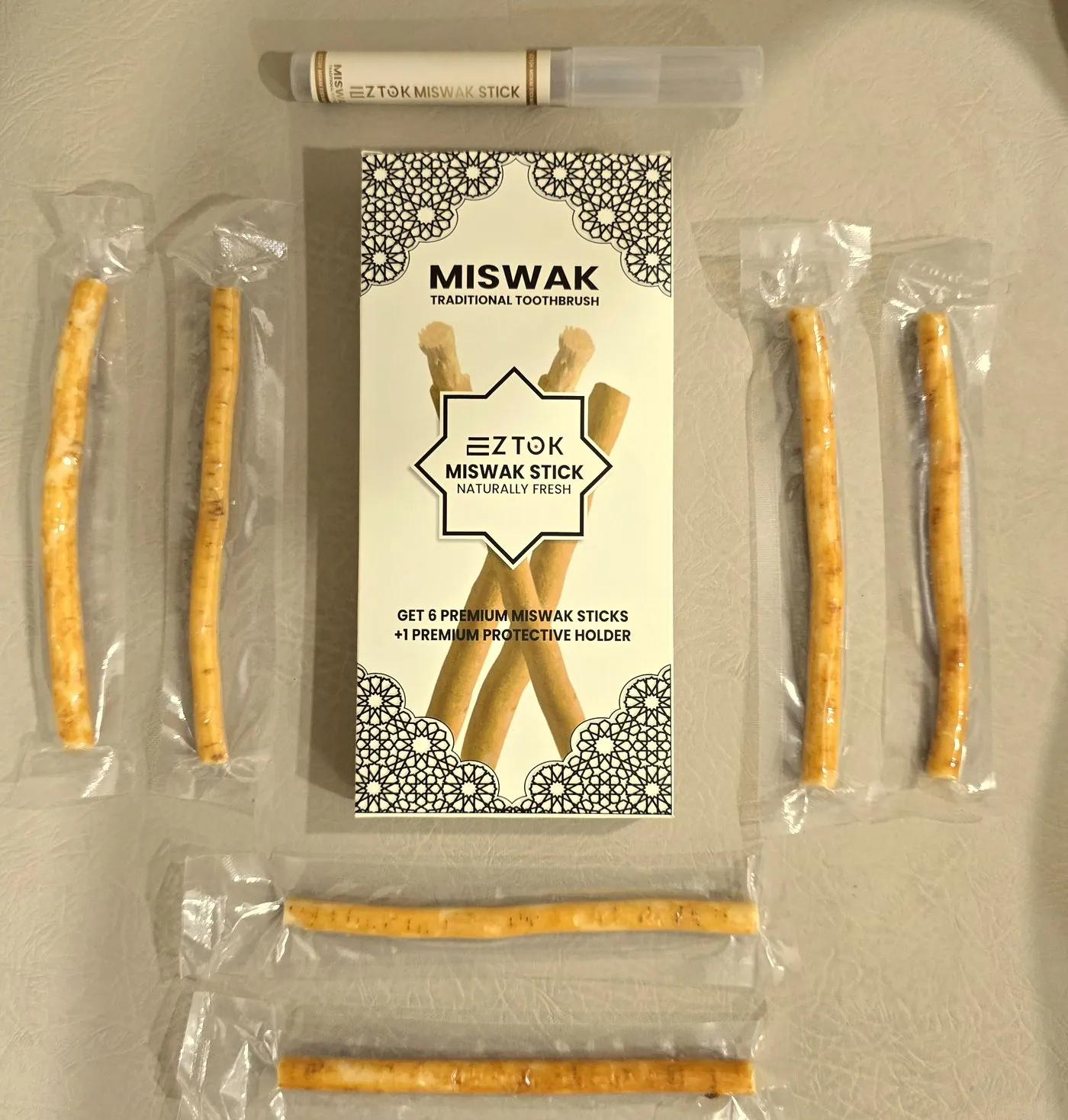 Six sealed miswak sticks laid symmetrically around a printed retail carton with a protective holder