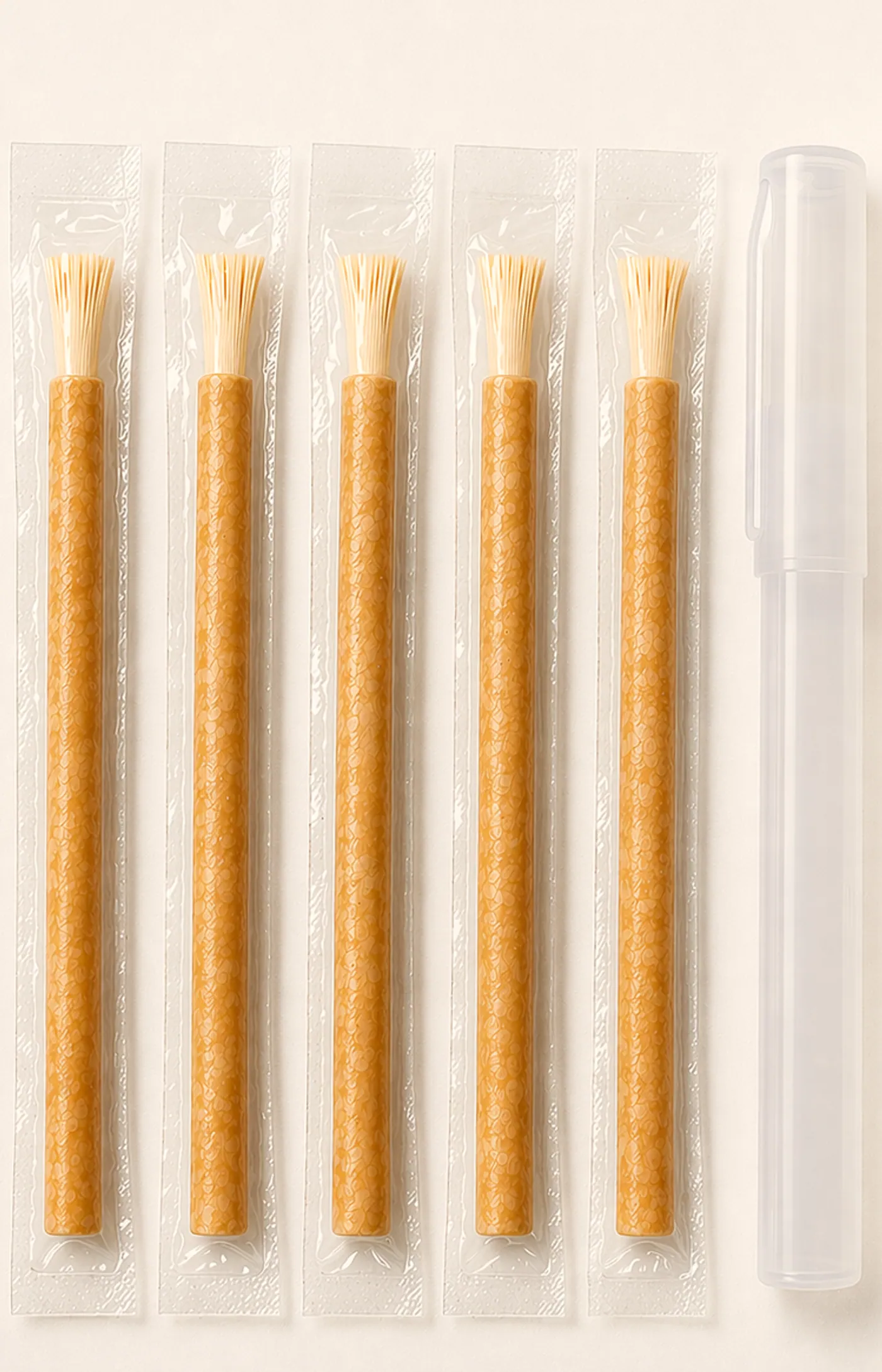 Five vacuum-sealed miswak sticks in a row beside a clear protective holder, photographed on a warm ivory ground