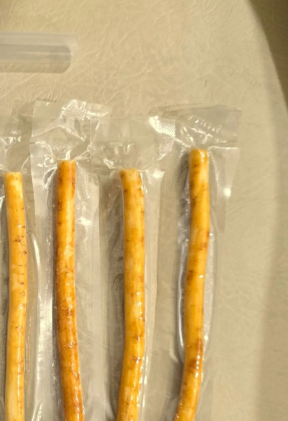 Four individually vacuum-sealed miswak sticks laid in a row on a cream ground